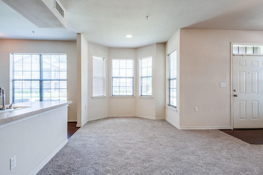 an empty living room with windows and a kitchen