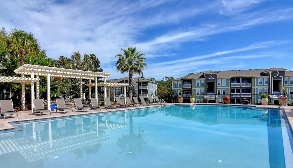 A large swimming pool with a white pergola and lounge chairs.