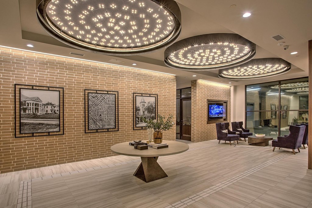 A modern office lobby with a round table and chairs, a flat screen TV, and framed pictures on the brick wall.