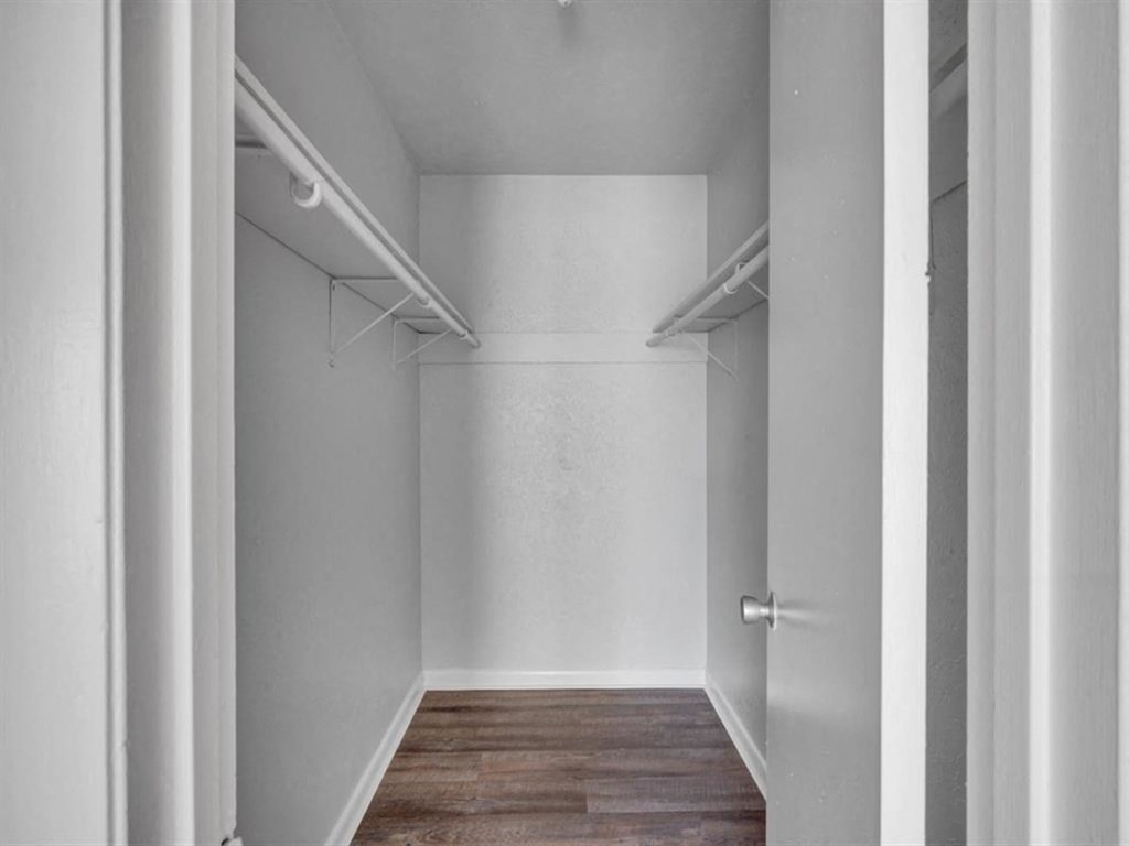 a walk in closet with white walls and a wood floor
