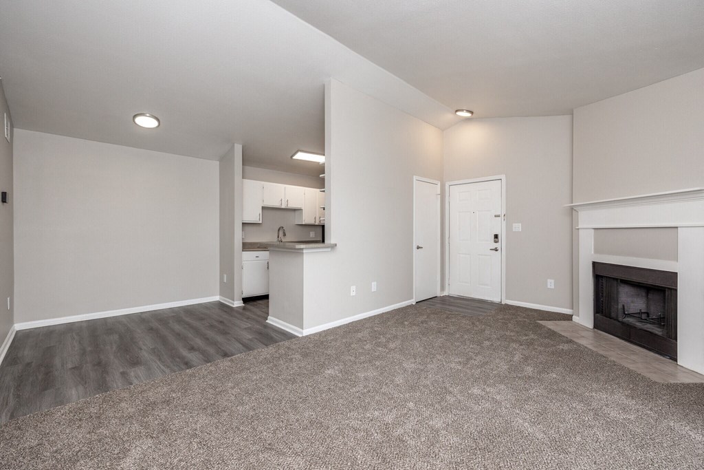 an empty living room with a fireplace and a kitchen