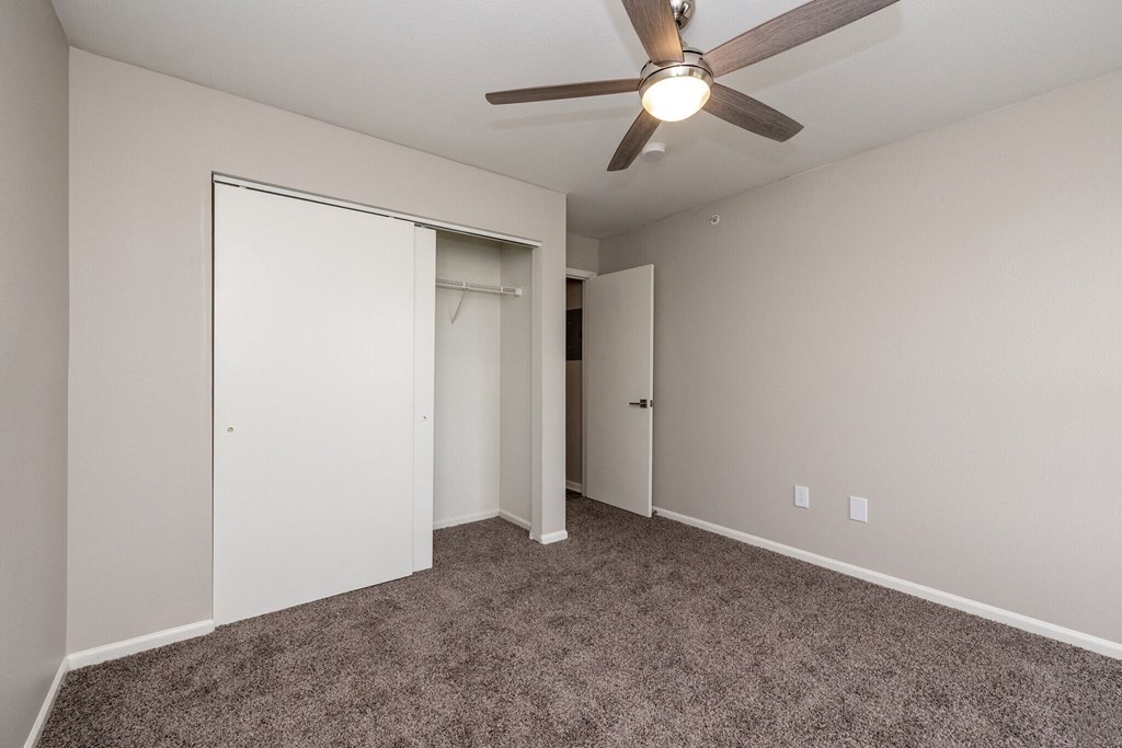 an empty bedroom with a ceiling fan and a closet