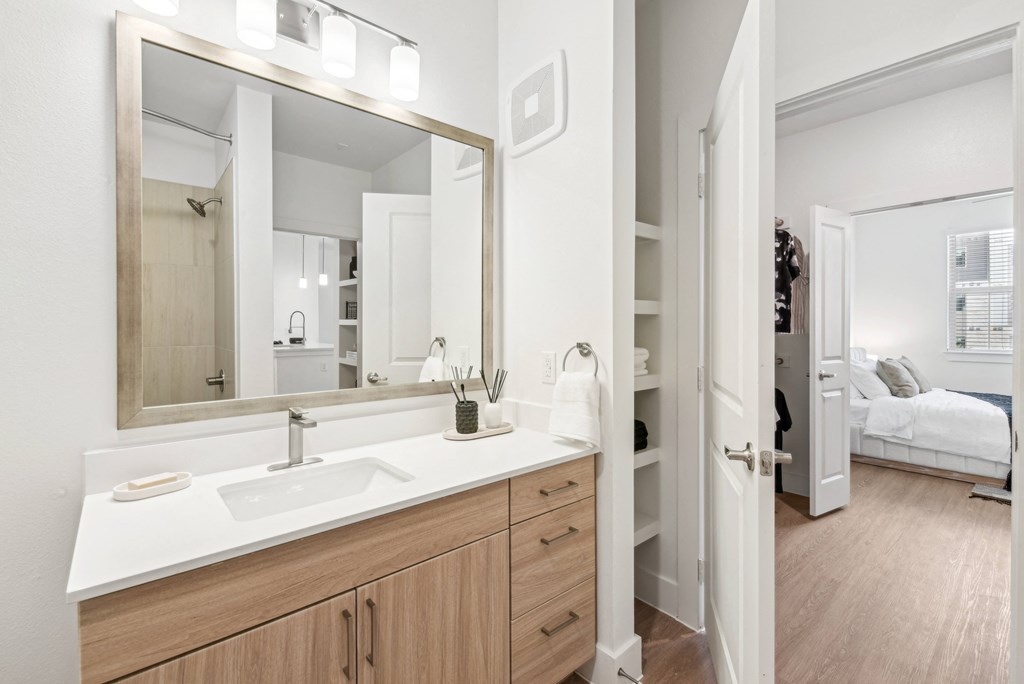 A bathroom with a sink, mirror, and a bedroom in the background.