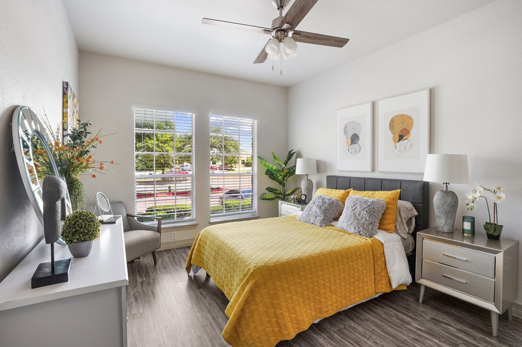 A bedroom with a yellow bedspread and a ceiling fan.