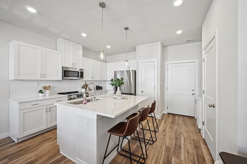 A kitchen with white cabinets and a white island with brown chairs.