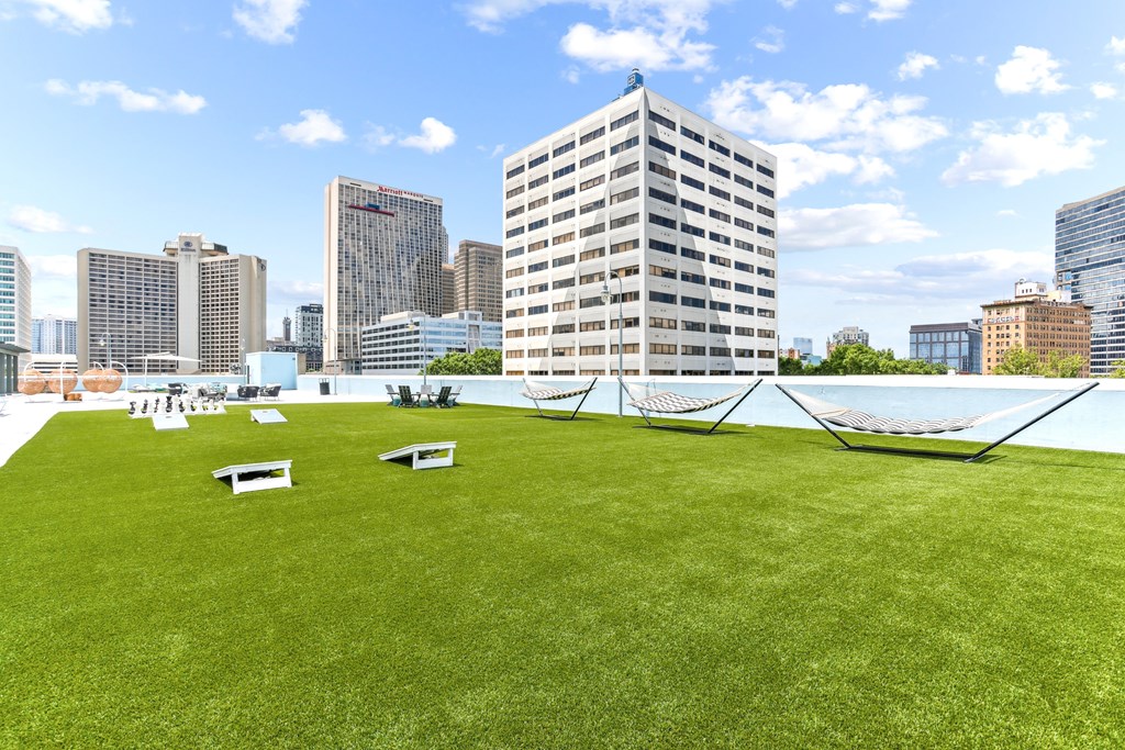 A grassy area with a hammock and benches in the foreground and a city skyline in the background.