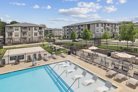 A swimming pool surrounded by sun loungers and apartment buildings.