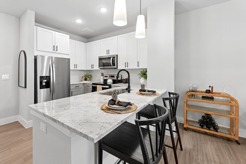 A kitchen with a marble countertop and black chairs.