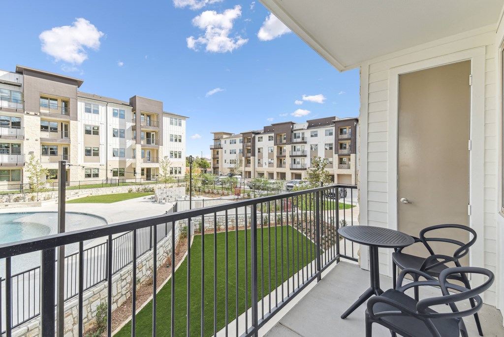 A balcony with a table and chairs overlooks a courtyard with a pool.