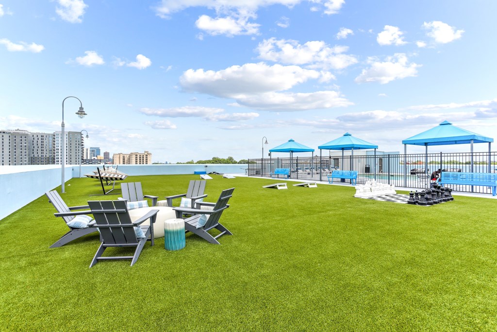 A lawn with chairs and umbrellas is in the foreground with a pool and apartment buildings in the background.