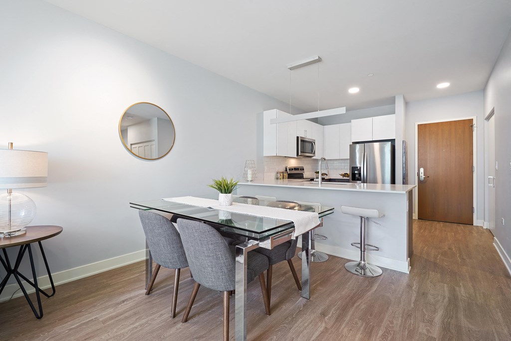 a dining area with a glass table and chairs and a kitchen in the background