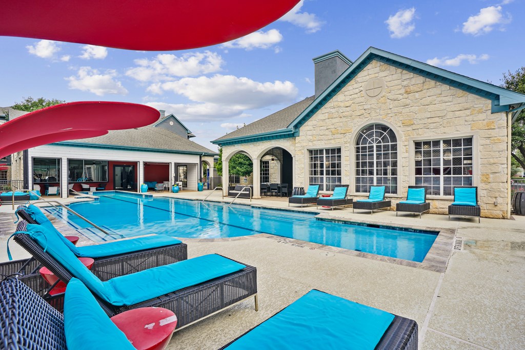 A large swimming pool with lounge chairs and a building in the background.