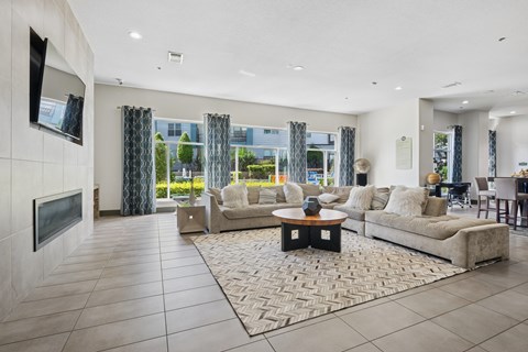 A modern living room with a large couch, a coffee table, and a flat-screen TV mounted on the wall.