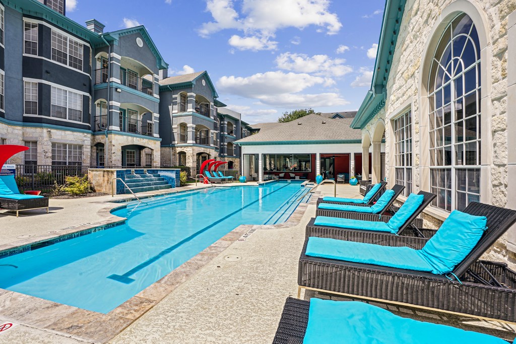 A large swimming pool with lounge chairs and a building in the background.