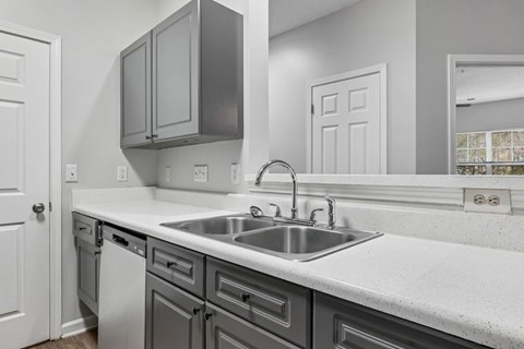 A kitchen with a white counter top and grey cabinets.