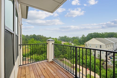 A balcony with a black railing and a wooden floor overlooks a green landscape.