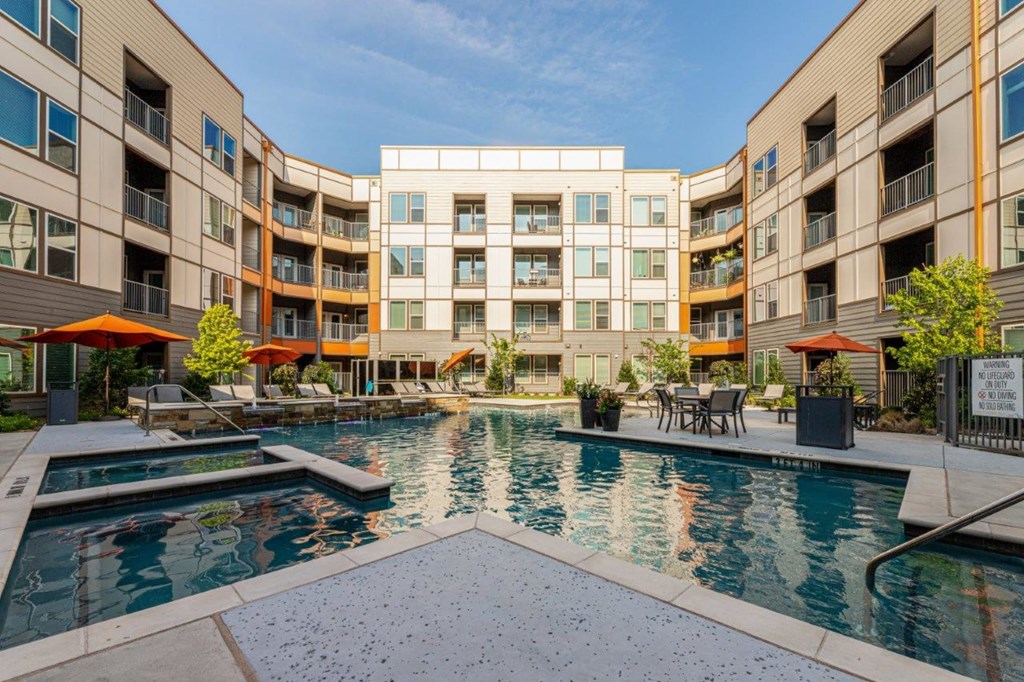 a swimming pool with umbrellas and tables in front of an apartment building