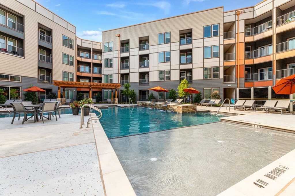 a swimming pool with lounge chairs and umbrellas in front of an apartment building