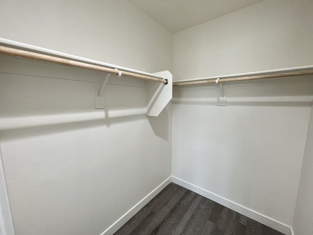 a walk in closet with white walls and a wooden floor