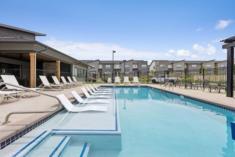 A swimming pool with lounge chairs and a fence in the background.