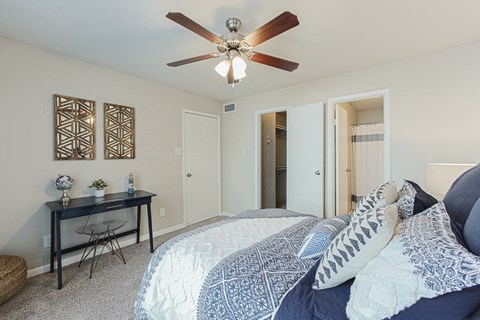 A bedroom with a bed, desk, and ceiling fan.