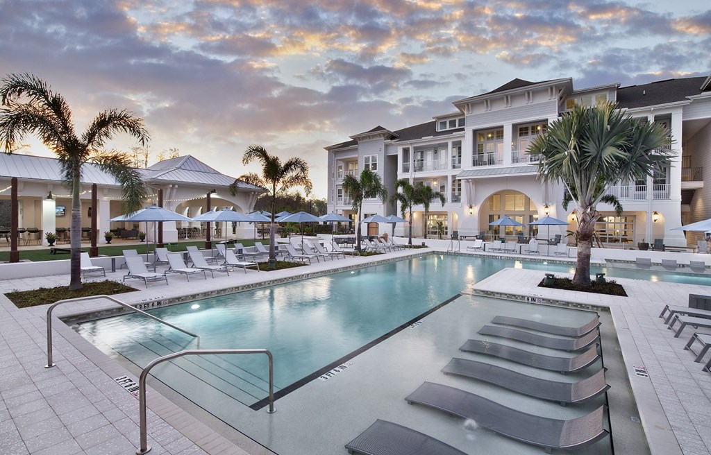 a large swimming pool with chaise lounge chairs and umbrellas in front of a large
