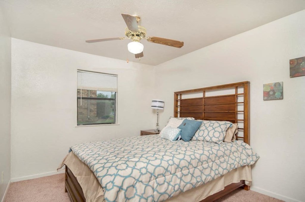 A bedroom with a bed, a ceiling fan, and a window with blinds.