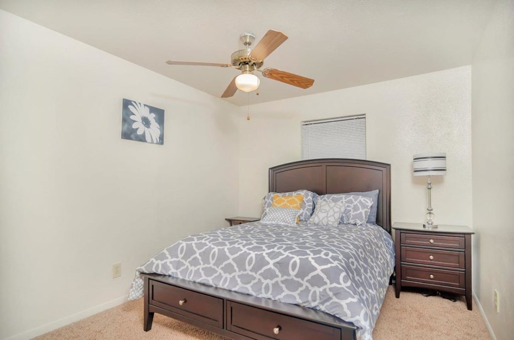 A bedroom with a bed, nightstand, and ceiling fan.