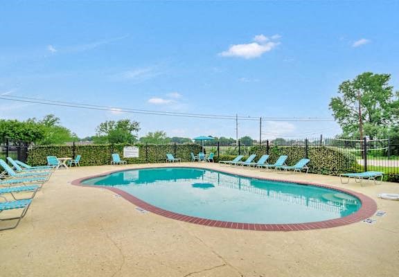 A round above ground pool surrounded by a black fence and chairs.