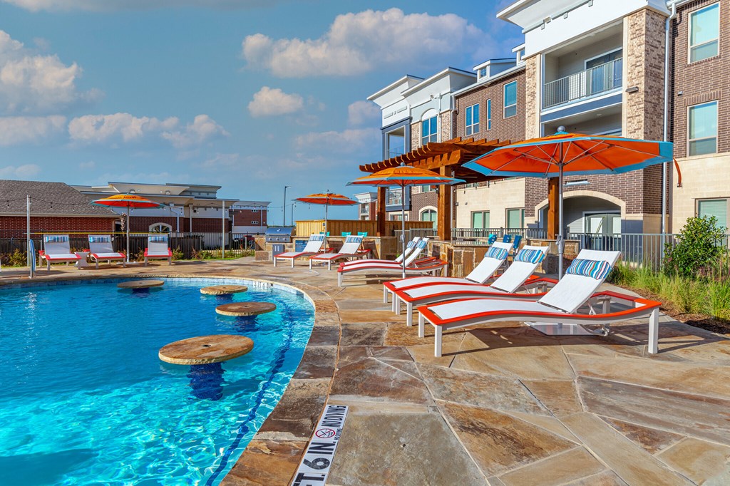 a swimming pool with chairs and umbrellas in front of an apartment building