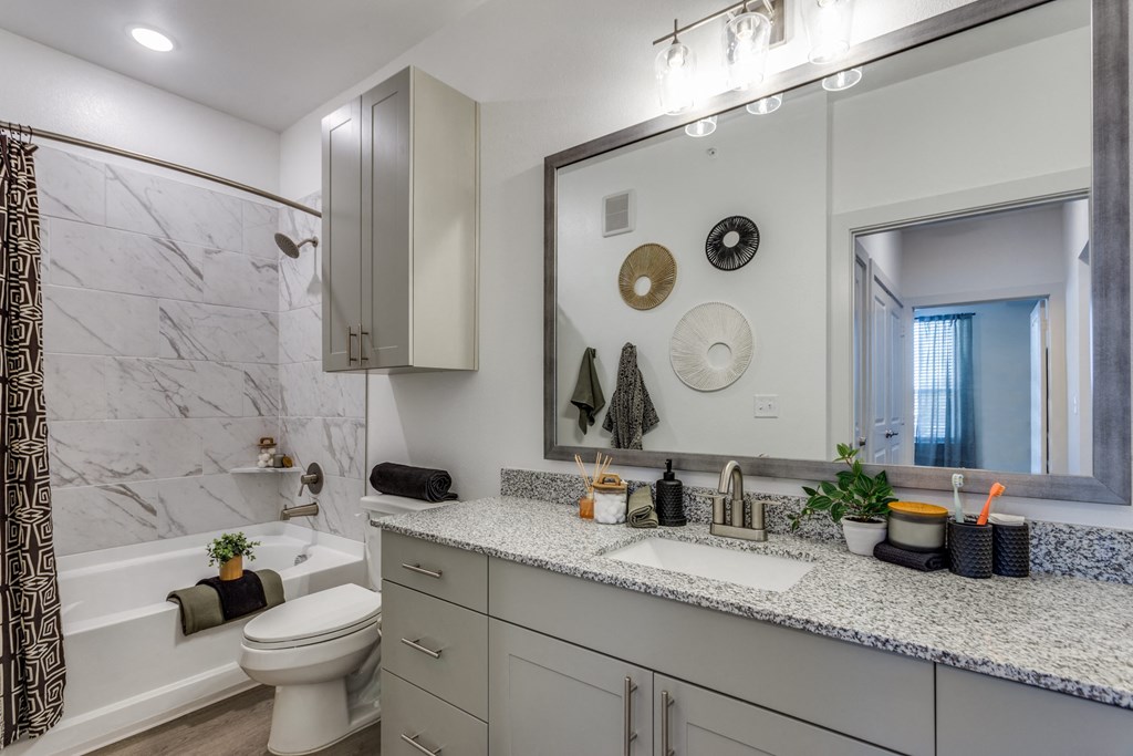 A bathroom with a marble tub surround and a large mirror above the sink.