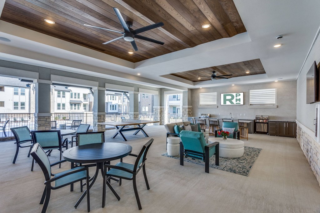 A large room with a table and chairs in the foreground and a balcony with chairs and tables in the background.