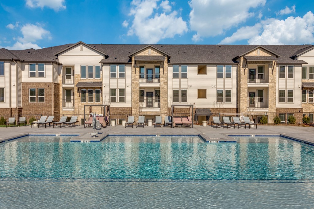 A large swimming pool in front of a building with lounge chairs around it.