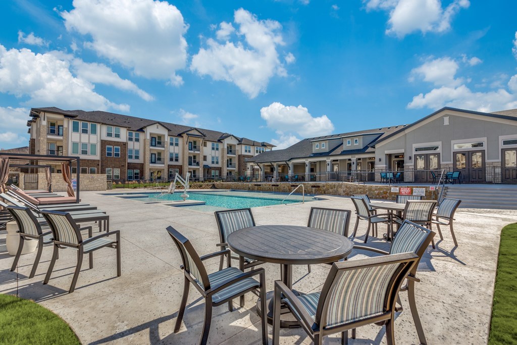 A sunny day at the outdoor pool area of a resort with chairs and tables arranged around the pool.