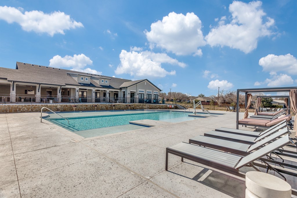 A swimming pool with sun loungers and a building in the background.