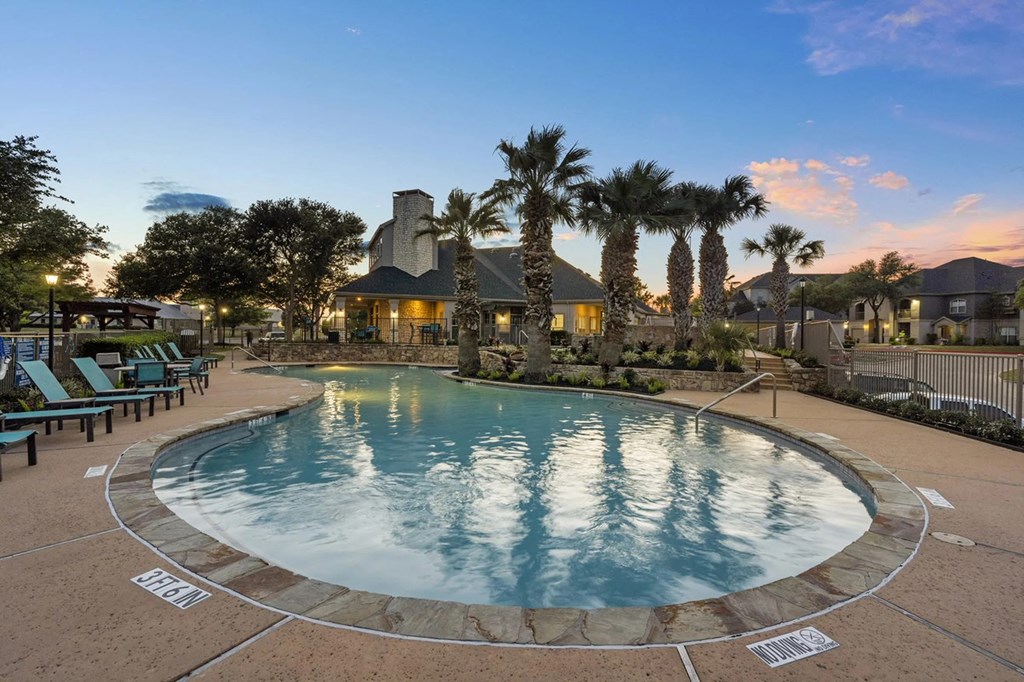 A large outdoor swimming pool surrounded by palm trees and lounge chairs.