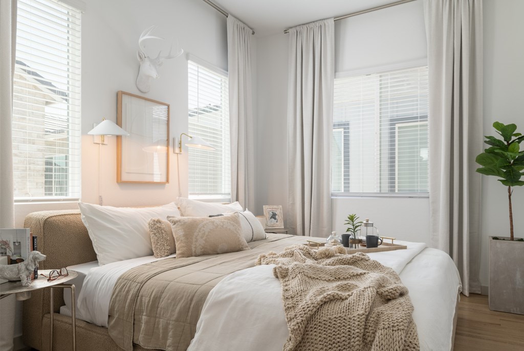 A bedroom with a large bed and a window with white curtains.