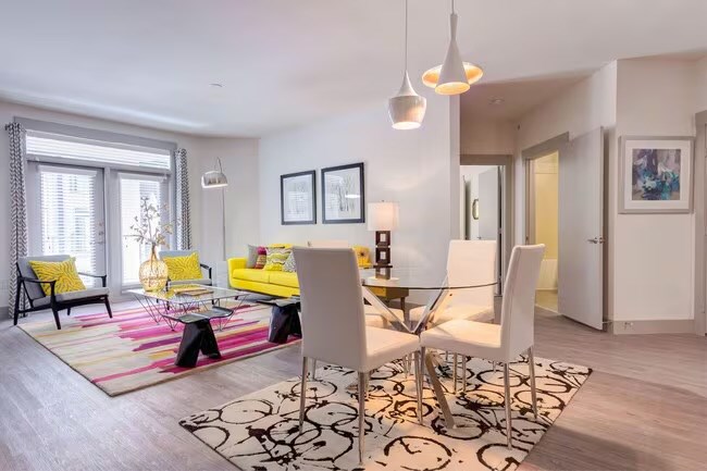 A modern living room with a yellow sofa, glass table, and a patterned rug.