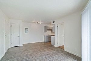 an empty living room with a kitchen in the background