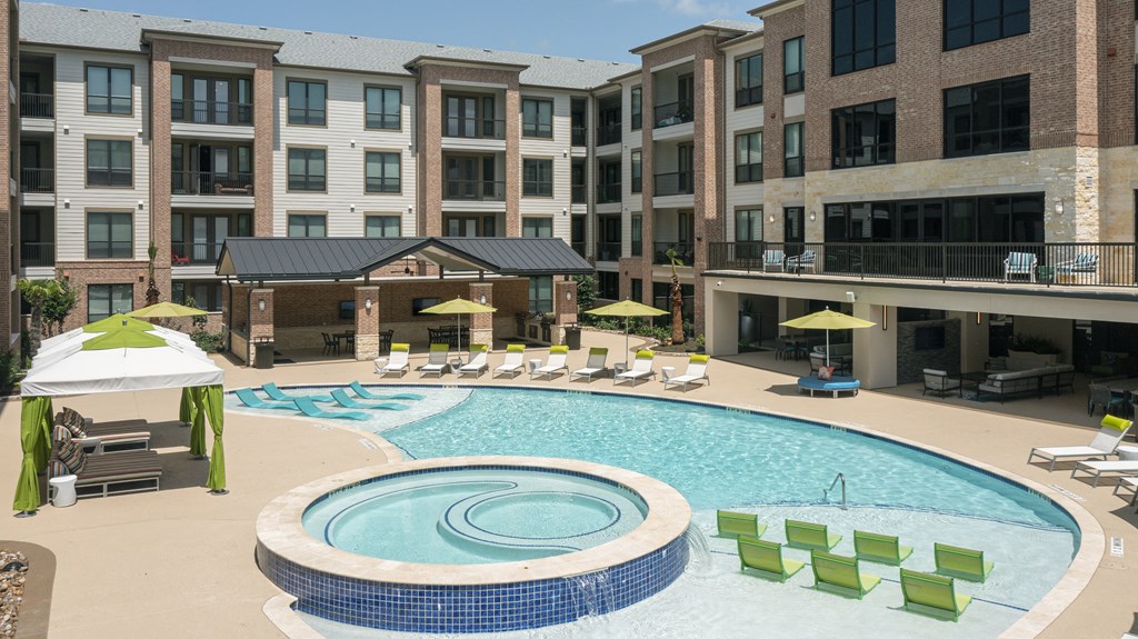 a large swimming pool with lounge chairs in front of an apartment building