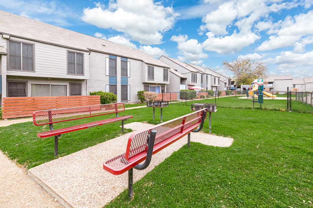 a park with benches and a playground in front of a row of houses