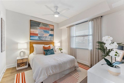A bedroom with a bed, a ceiling fan, and a painting on the wall.