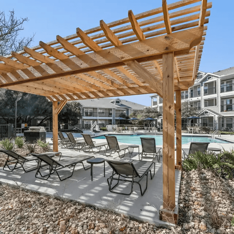 A wooden pergola over a poolside lounge area.