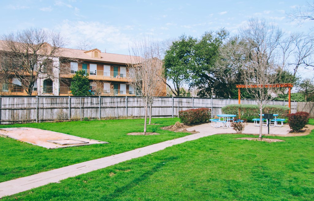 a yard with a picnic area and a fence with an apartment building in the background