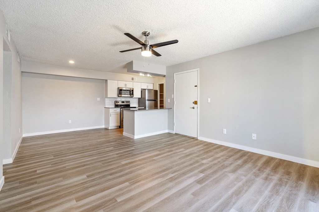 an empty living room with a ceiling fan and a kitchen