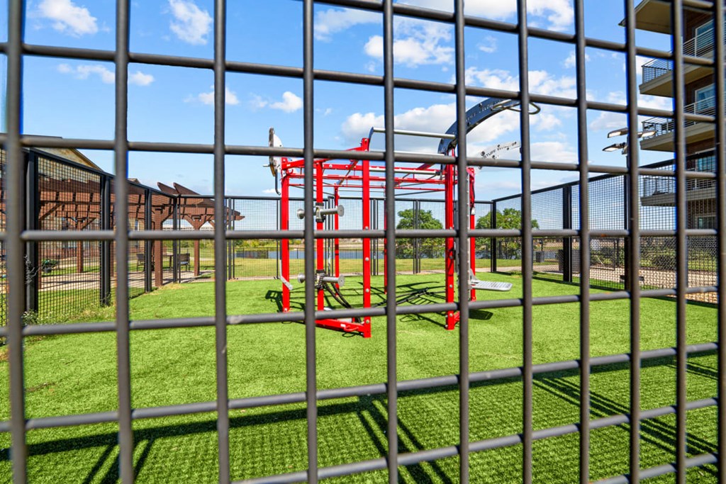 A playground with a red swing set is seen through a metal fence.