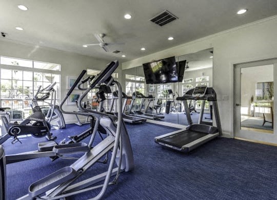 a gym with cardio equipment and a television