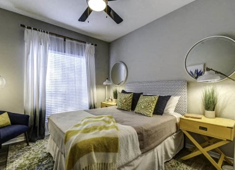 A bedroom with a bed, a chair, a table, and a ceiling fan.