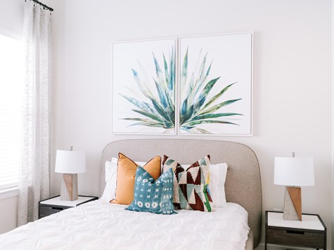A bedroom with a bed, two lamps, and a painting of a plant.