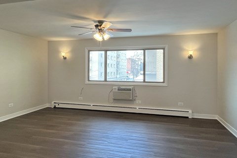 A room with a ceiling fan and a window with a view of a street.
